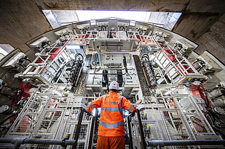 A person standing in PPE in front of a tunnel boring machine
