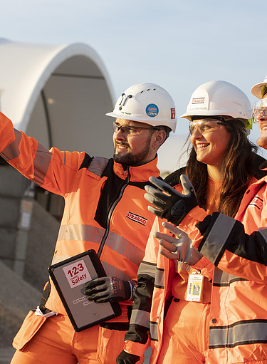Three people on a construction site with one pointing into the distance