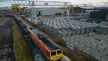 A train being loaded with tunnel segments with the yard of completed segments behind