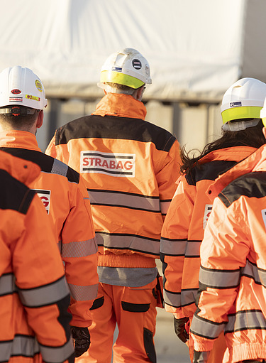 People in STRABAG PPE on site walking away from the camera