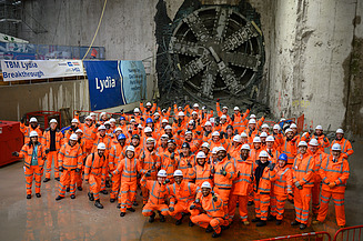Large group of people in PPE gathered celebrating with the tunnel boring machine in the background 