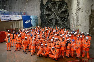 Large group of people in PPE gathered celebrating with the tunnel boring machine in the background 