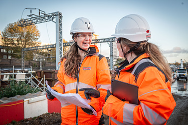 Two women on a construction site having a conversation while looking at plans 