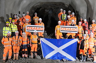 Group of people in PPE standing together holding the STRABAG logo and a Scottish flag 