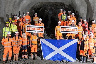 Group of people in PPE standing together holding the STRABAG logo and a Scottish flag 