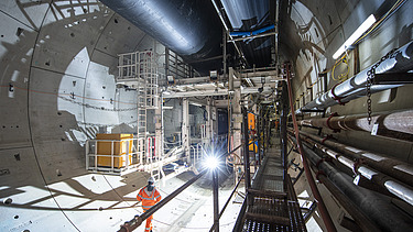 Person walking along a concrete segment lined tunnel at the back of a TBM 