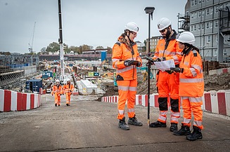 Two women and a man on a HS2 construction site with two men in the background