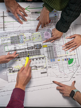 Several pairs of hands pointing to a plan 