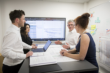 Four poeple having a meeting gathered around a table with a screen in the background 